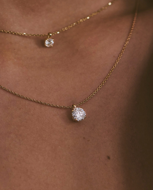 Close up of someone wearing layered gold necklaces with round natural diamond pendants