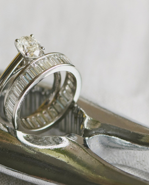 A white gold engagement ring with an oval-cut natural diamond and matching baguette diamond wedding band, displayed on a metallic ring sizer.